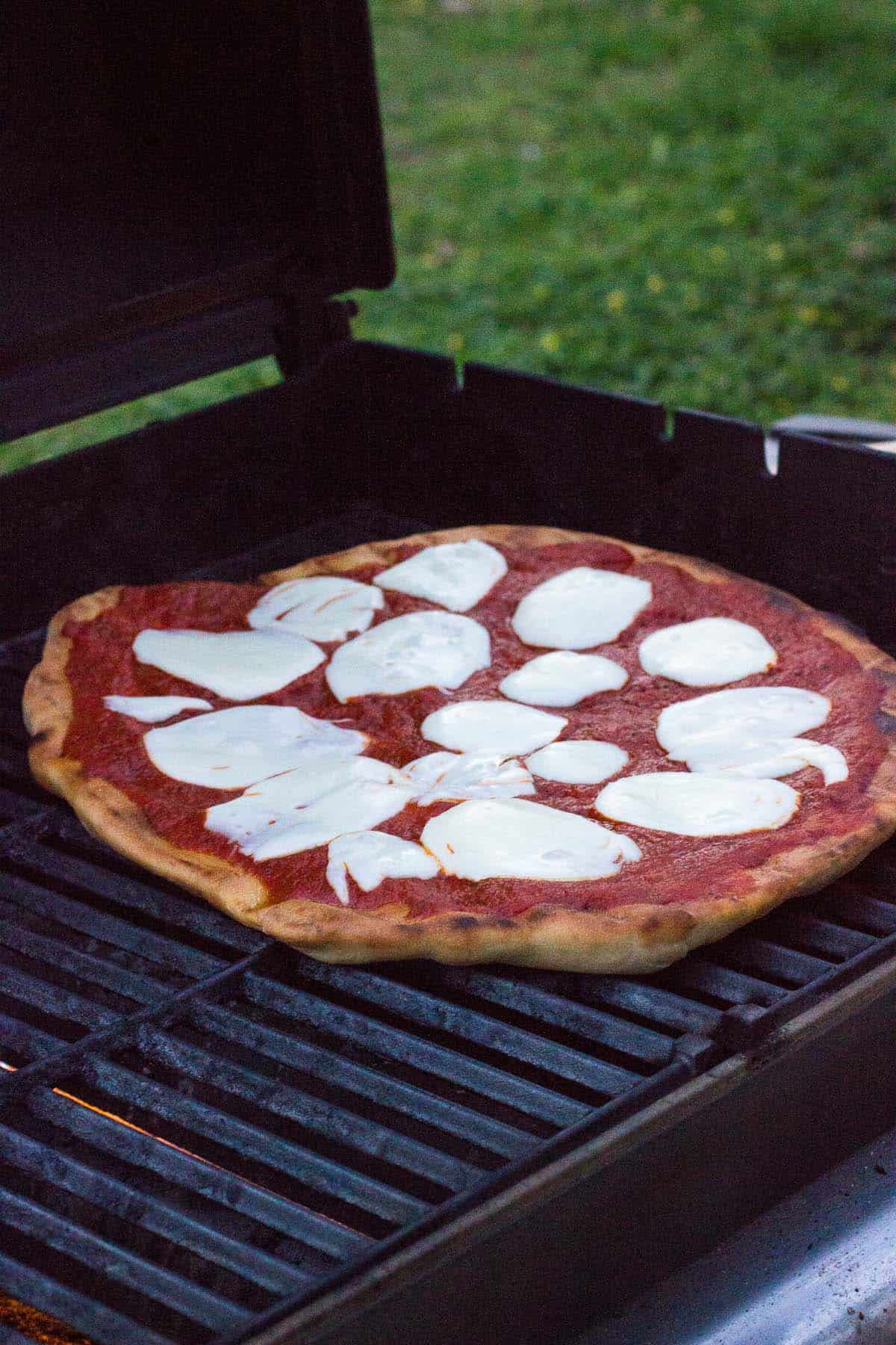 Pizza on the grill with sauce and melted mozzarella cheese.