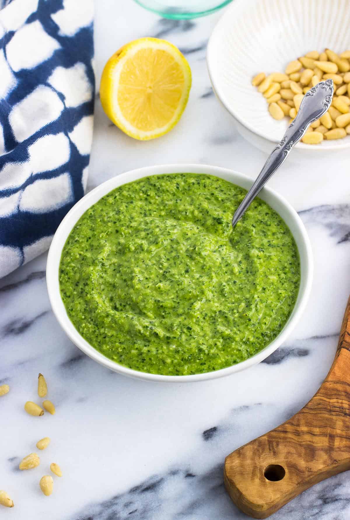 A bowl of spinach pesto with a spoon in it.