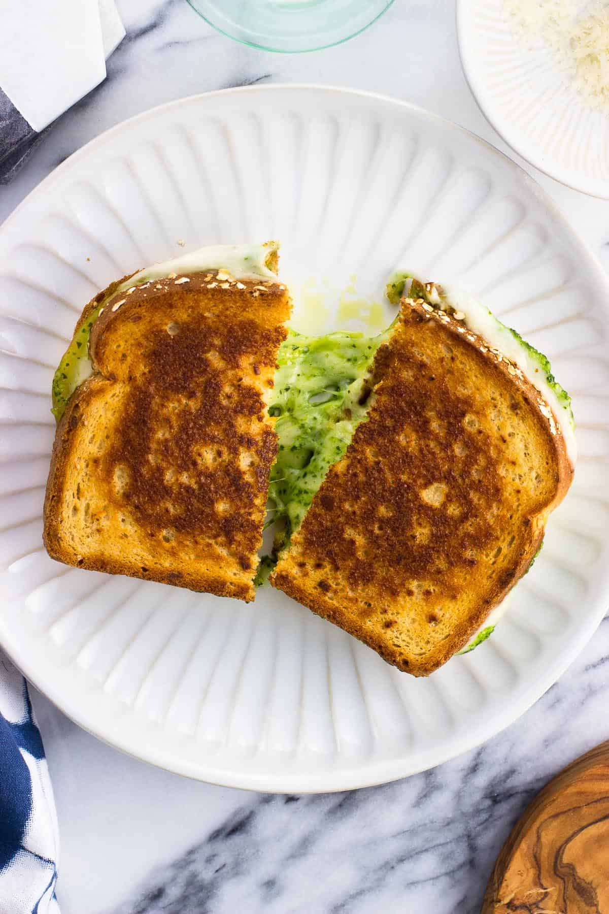 A pesto grilled cheese cut in half on a plate.