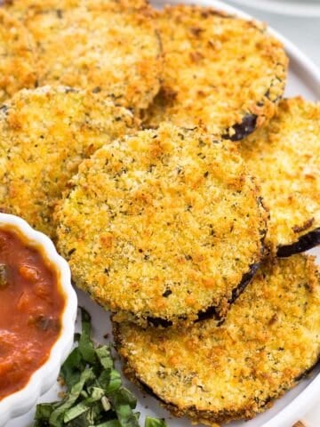 Air fried eggplant rounds on a plate with a bowl of marinara dipping sauce.