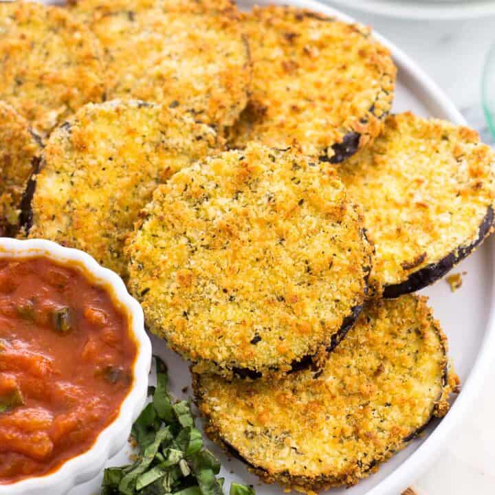 Air fried eggplant rounds on a plate with a bowl of marinara dipping sauce.