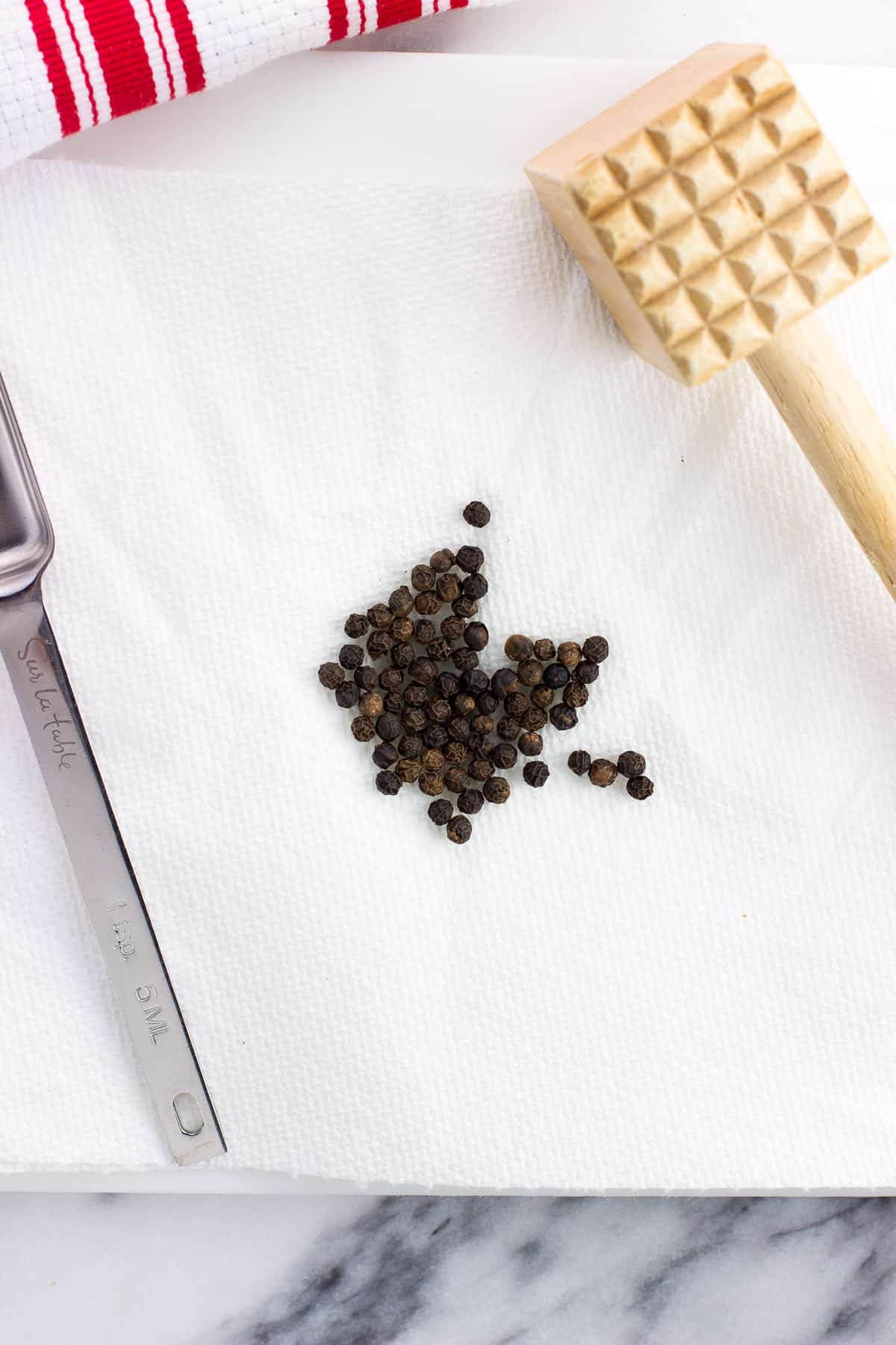 Whole peppercorns on a paper towel next to a meat tenderizer.