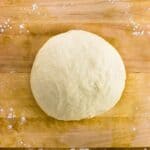 A ball of pizza dough on a wooden cutting board.