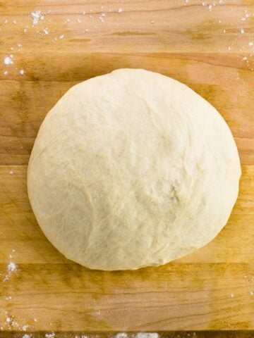A ball of pizza dough on a wooden cutting board.