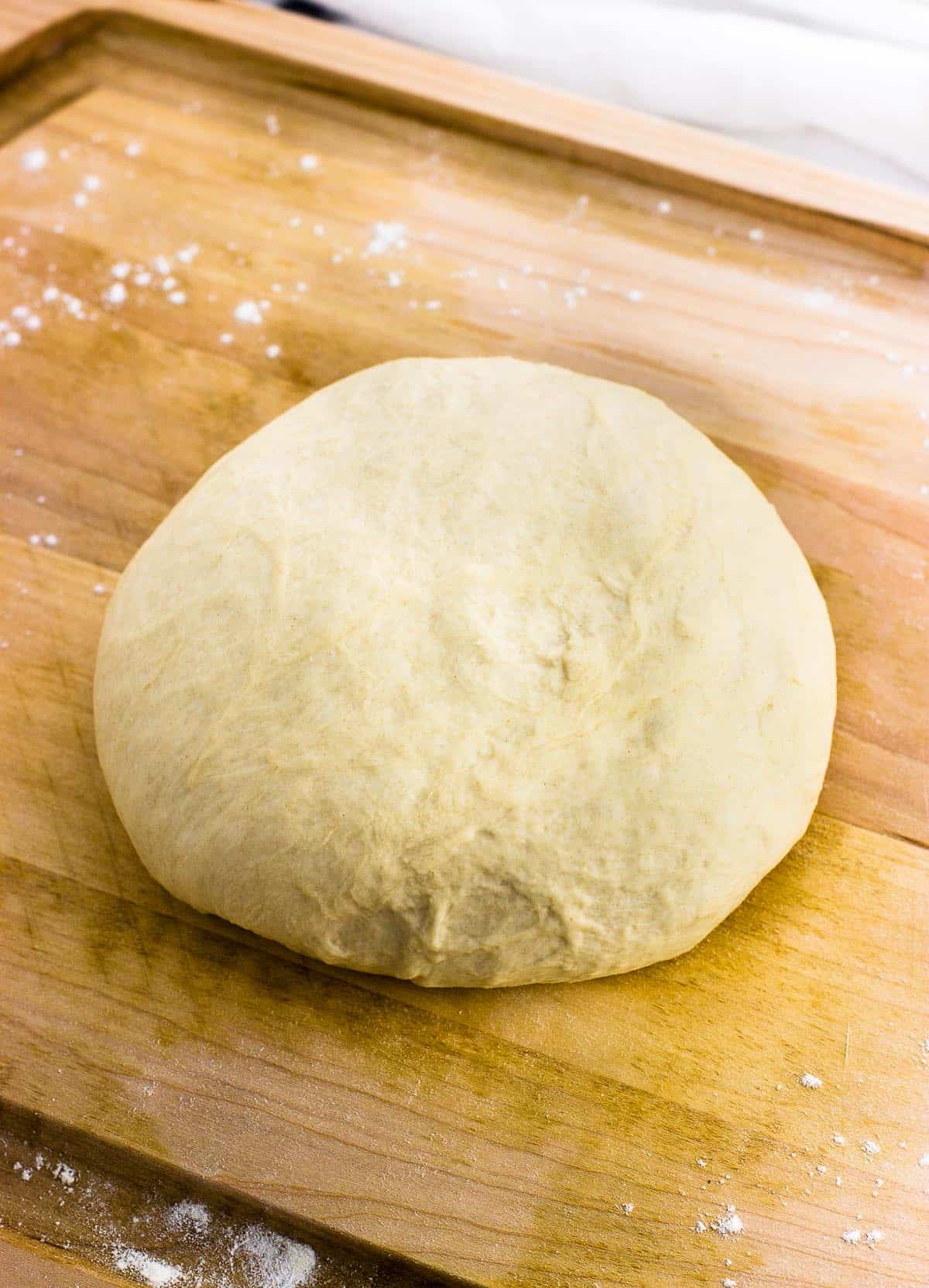 A ball of pizza dough on a wooden cutting board.