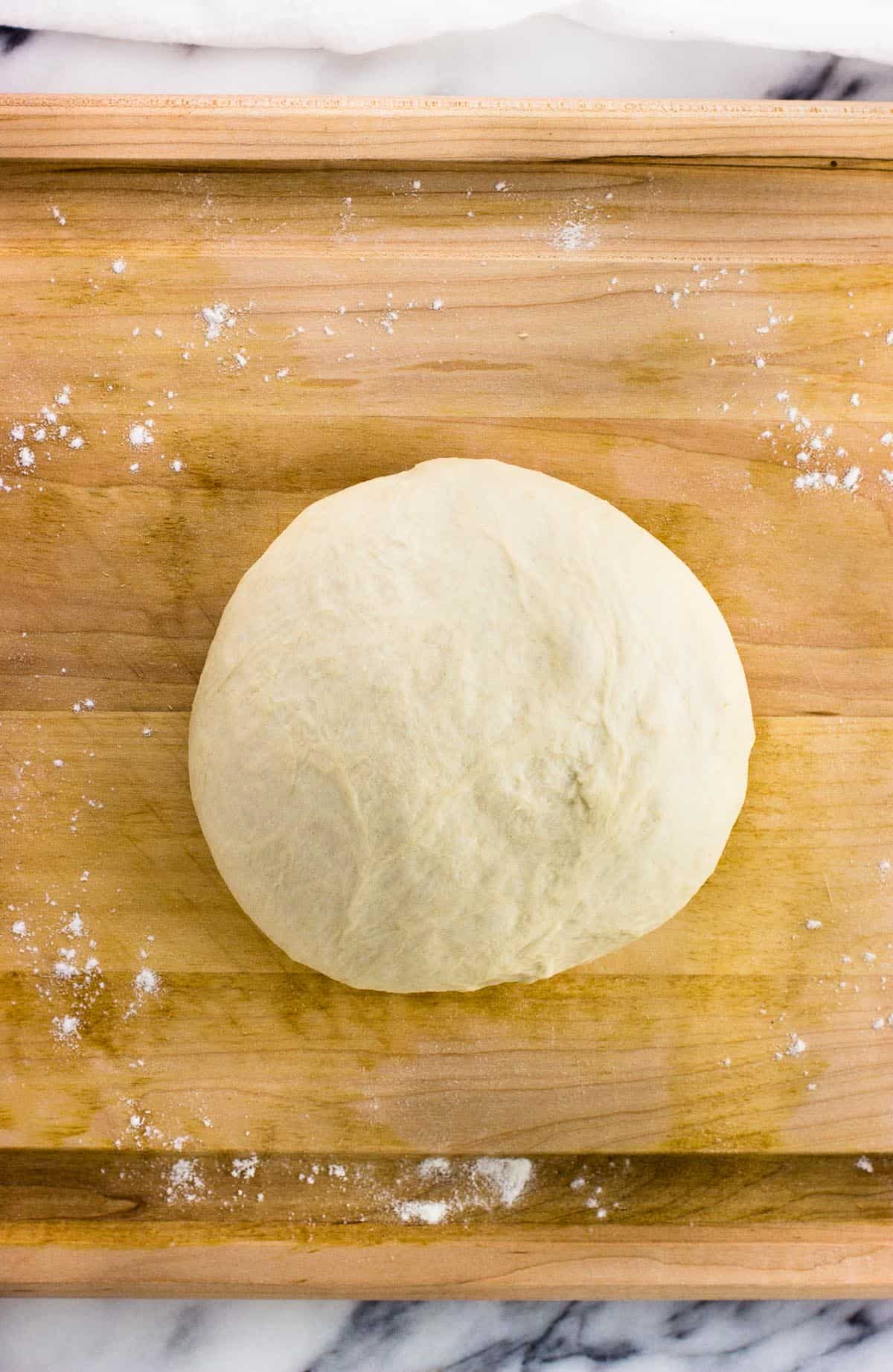 A ball of pizza dough on a wooden cutting board.