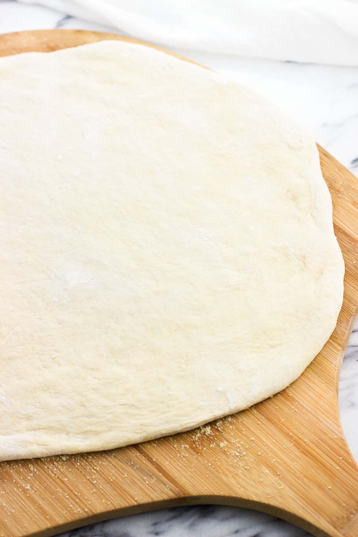 A stretched out pizza crust raw on a wooden peel.