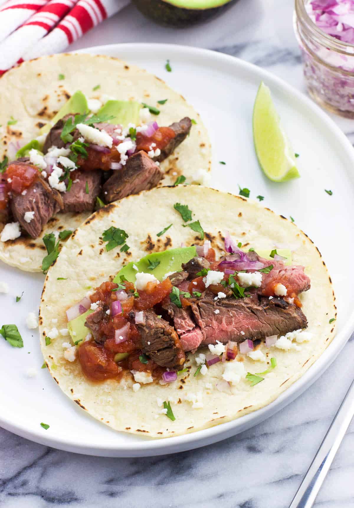 Two all-dressed carne asada tacos on a plate.