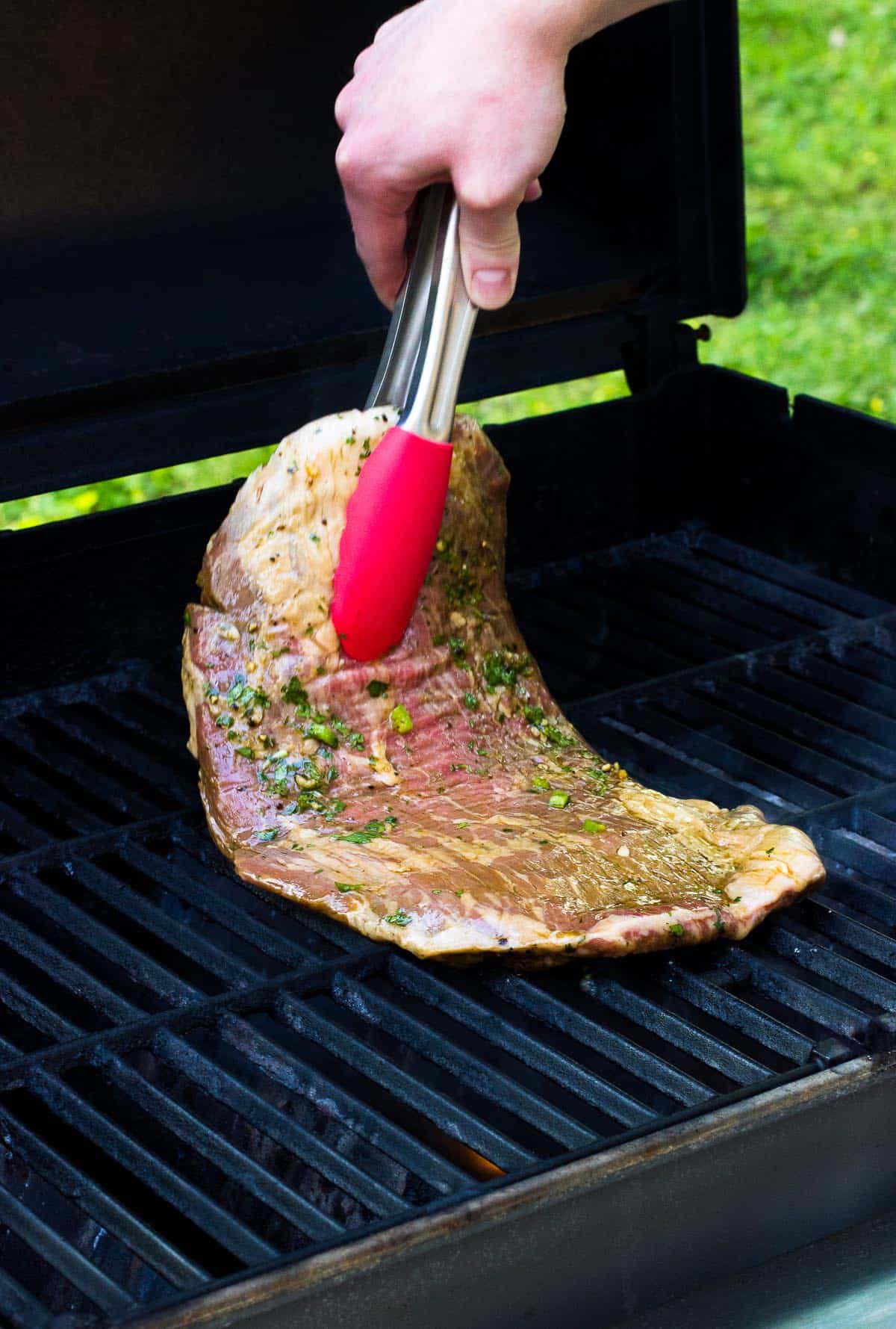 A raw slab of steak being laid on the grill with tongs.