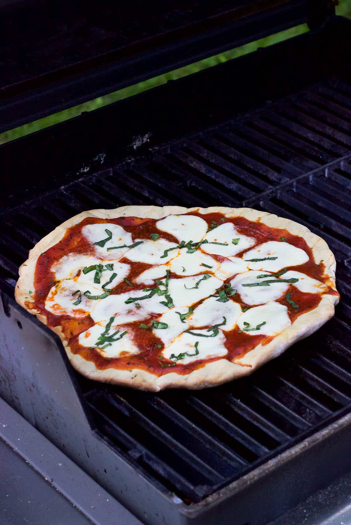 A grilled pizza on the grill just prior to be removed to serve.