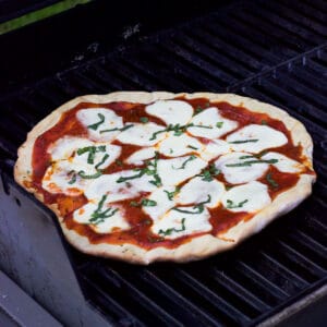 A grilled pizza on the grill just prior to be removed to serve.