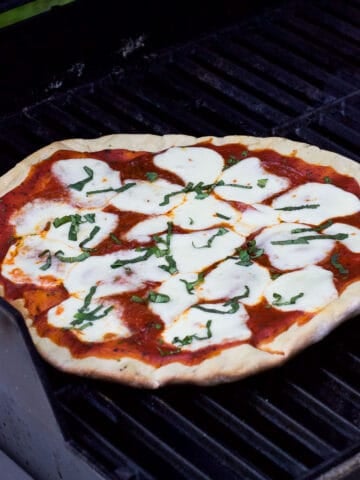 A grilled pizza on the grill just prior to be removed to serve.
