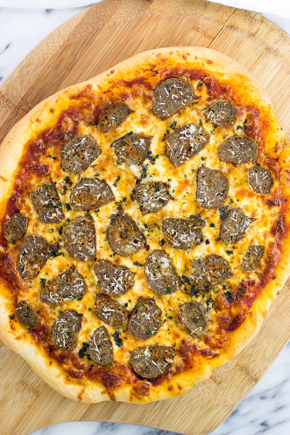 A cooked meatball pizza on a wooden peel.