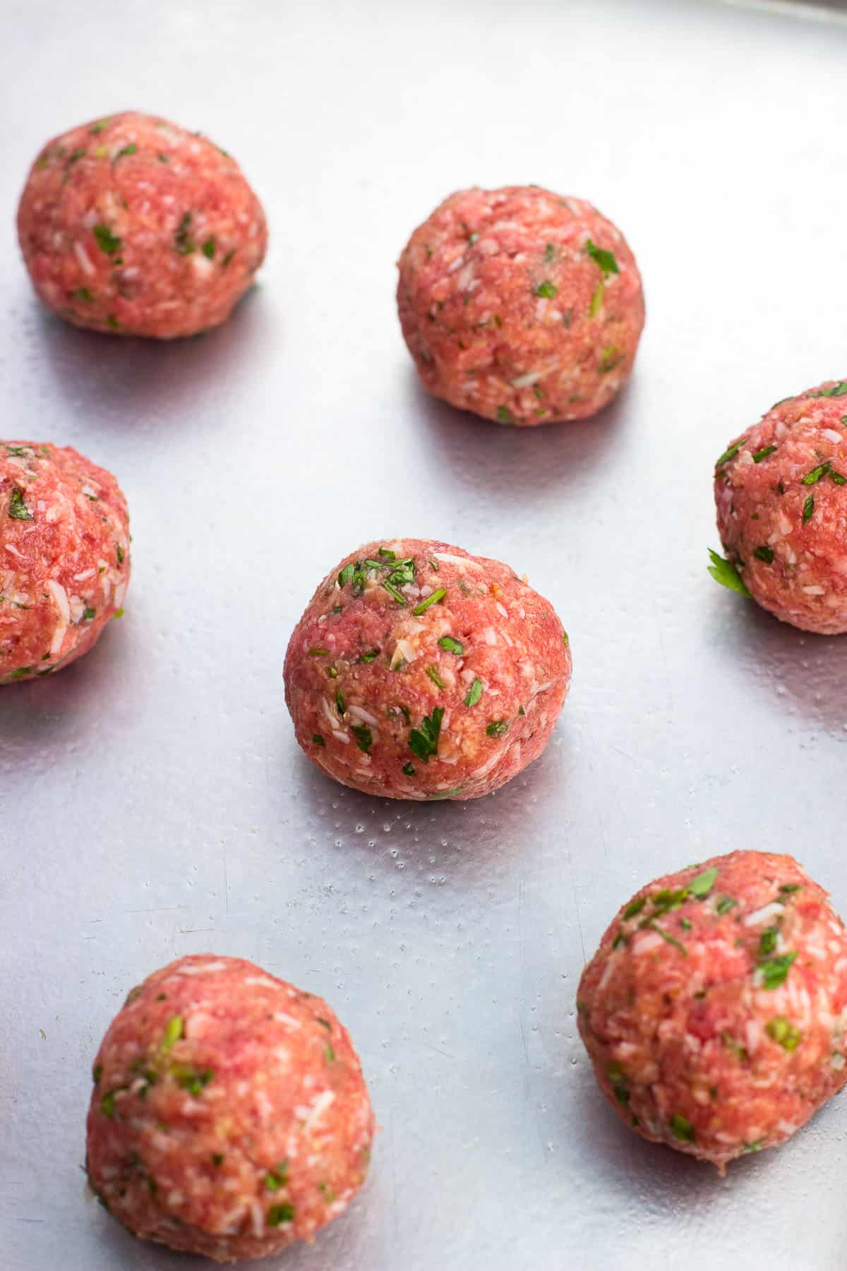 Raw meatballs shaped on a sheet pan.