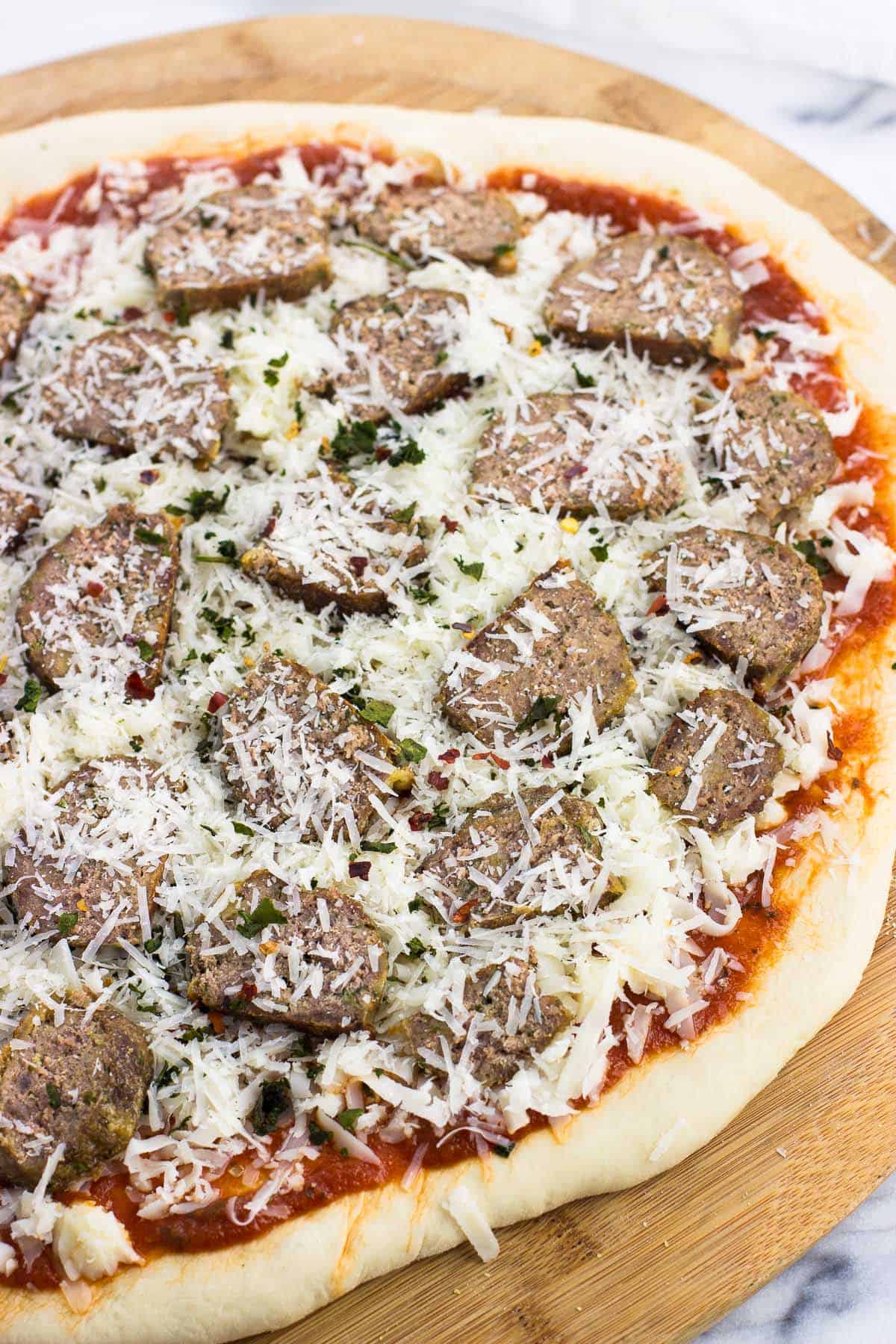 Meatball pizza on a wooden peel before going in the oven.