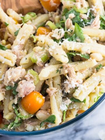 A close-up of a bowl of tuna pasta salad with a wooden serving spoon.