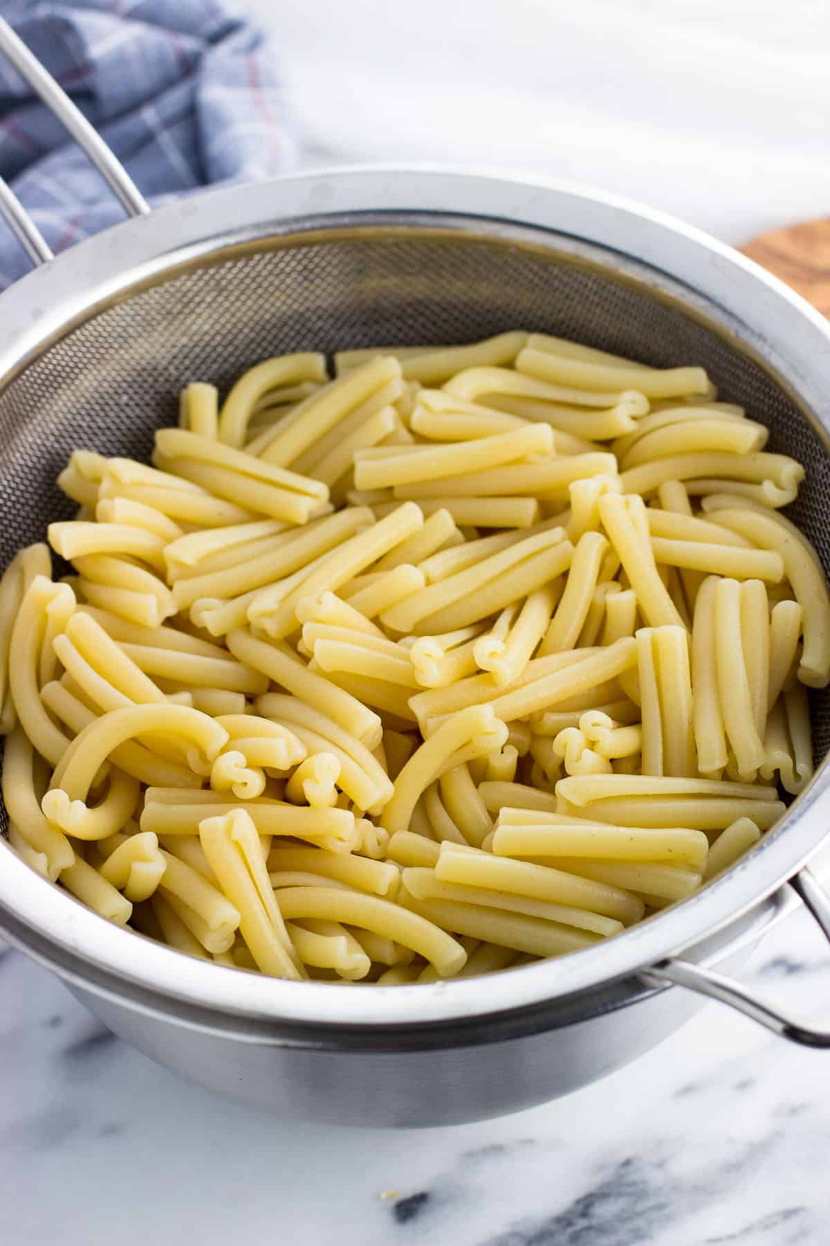 Drained pasta in a large strainer set over a bowl.