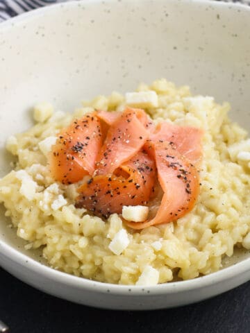 A shallow bowl of risotto topped with smoked salmon slices.