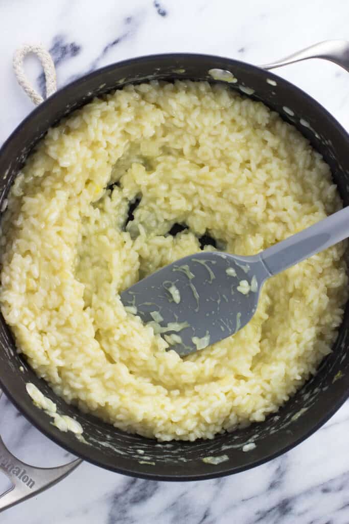 Risotto getting creamy in the pan with a spatula.