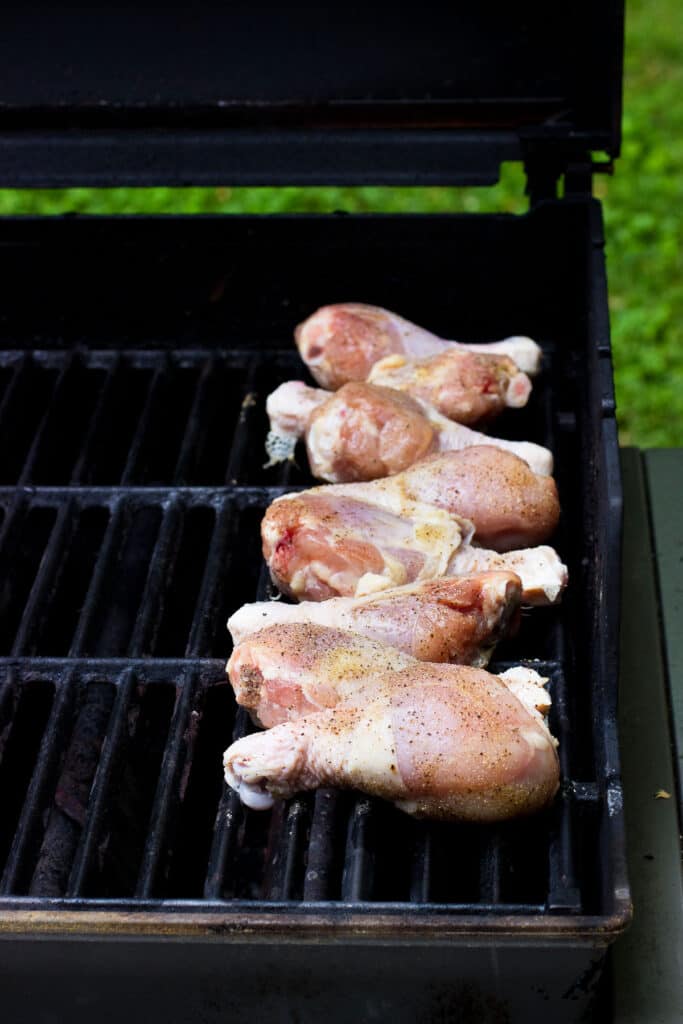 Raw chicken drumsticks lined up on the grill.