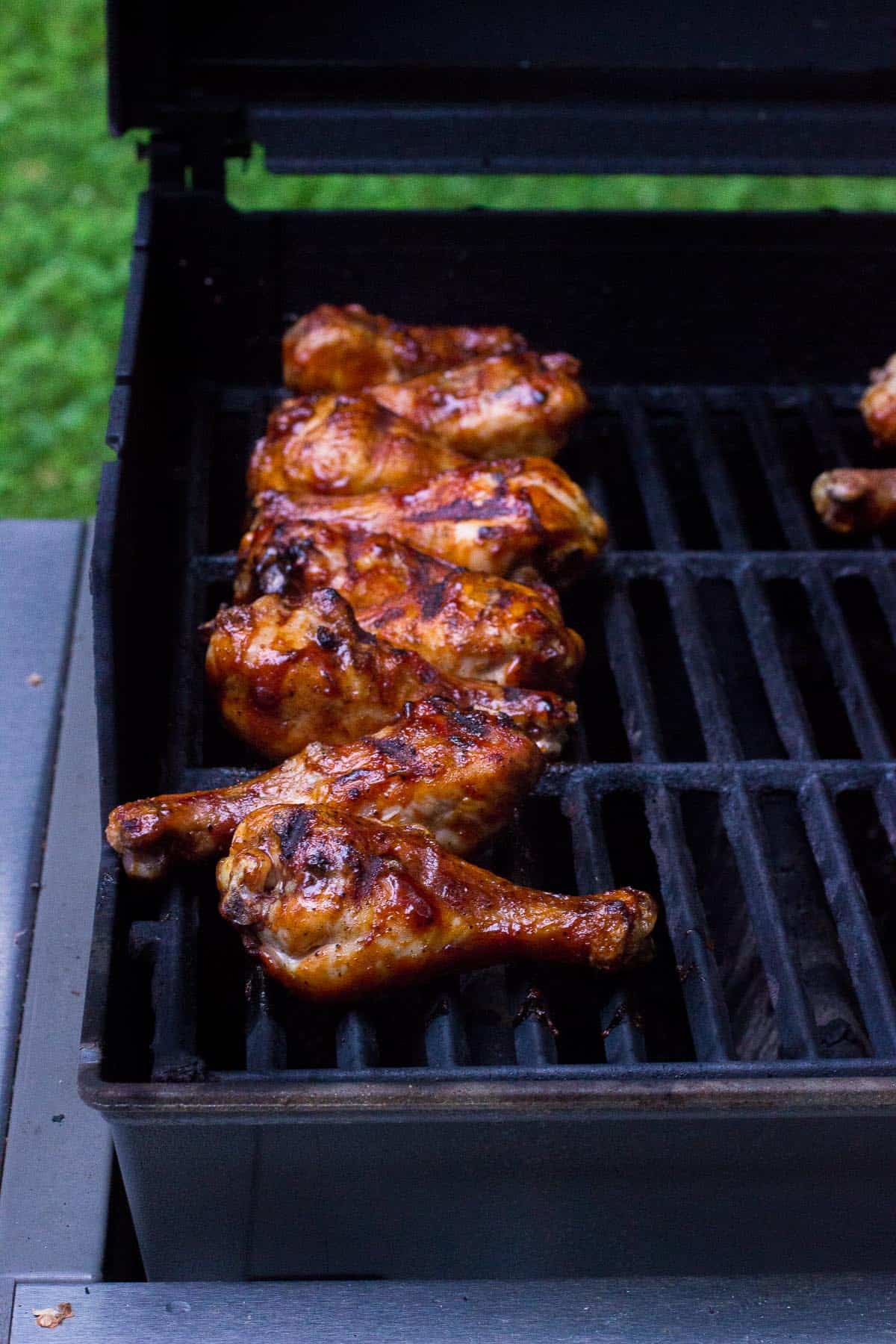 Grilled and basted chicken drumsticks lined up on the grill.