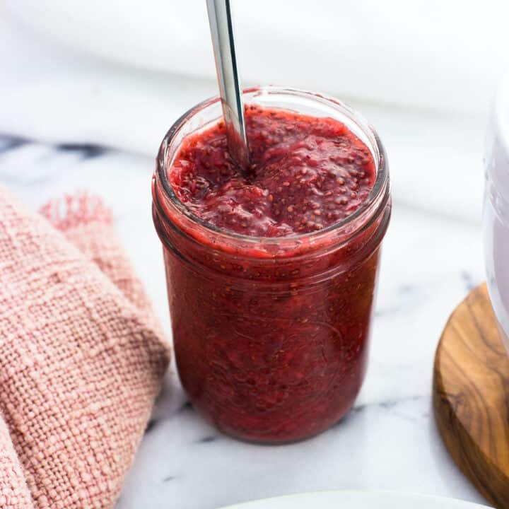A jar of strawberry chia jam with a spoon in it.