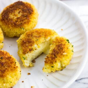 Risotto cakes on a plate with one cut in half to show melted cheese.