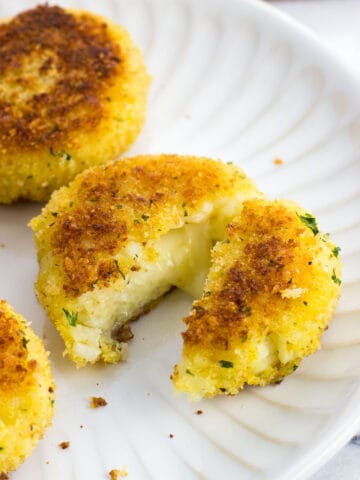 Risotto cakes on a plate with one cut in half to show melted cheese.