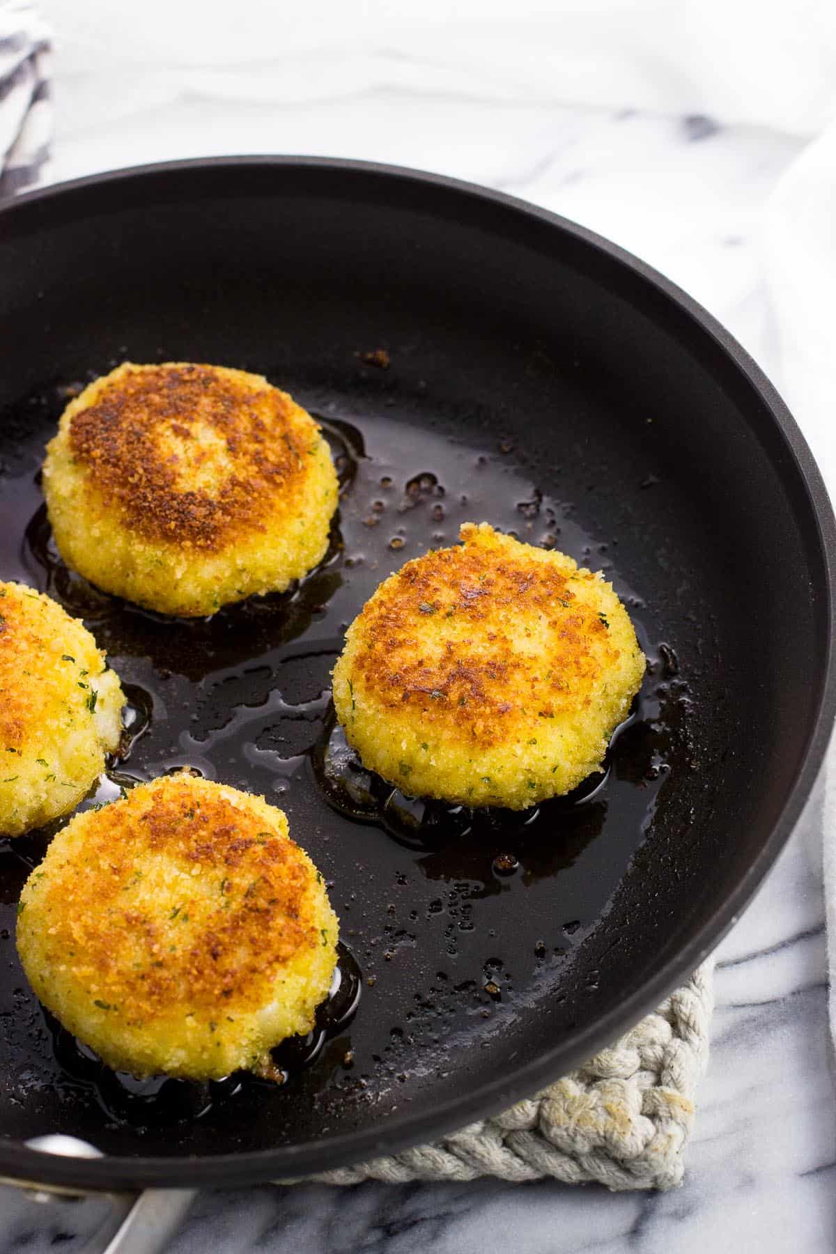 Four pan-fried risotto cakes in a skillet.
