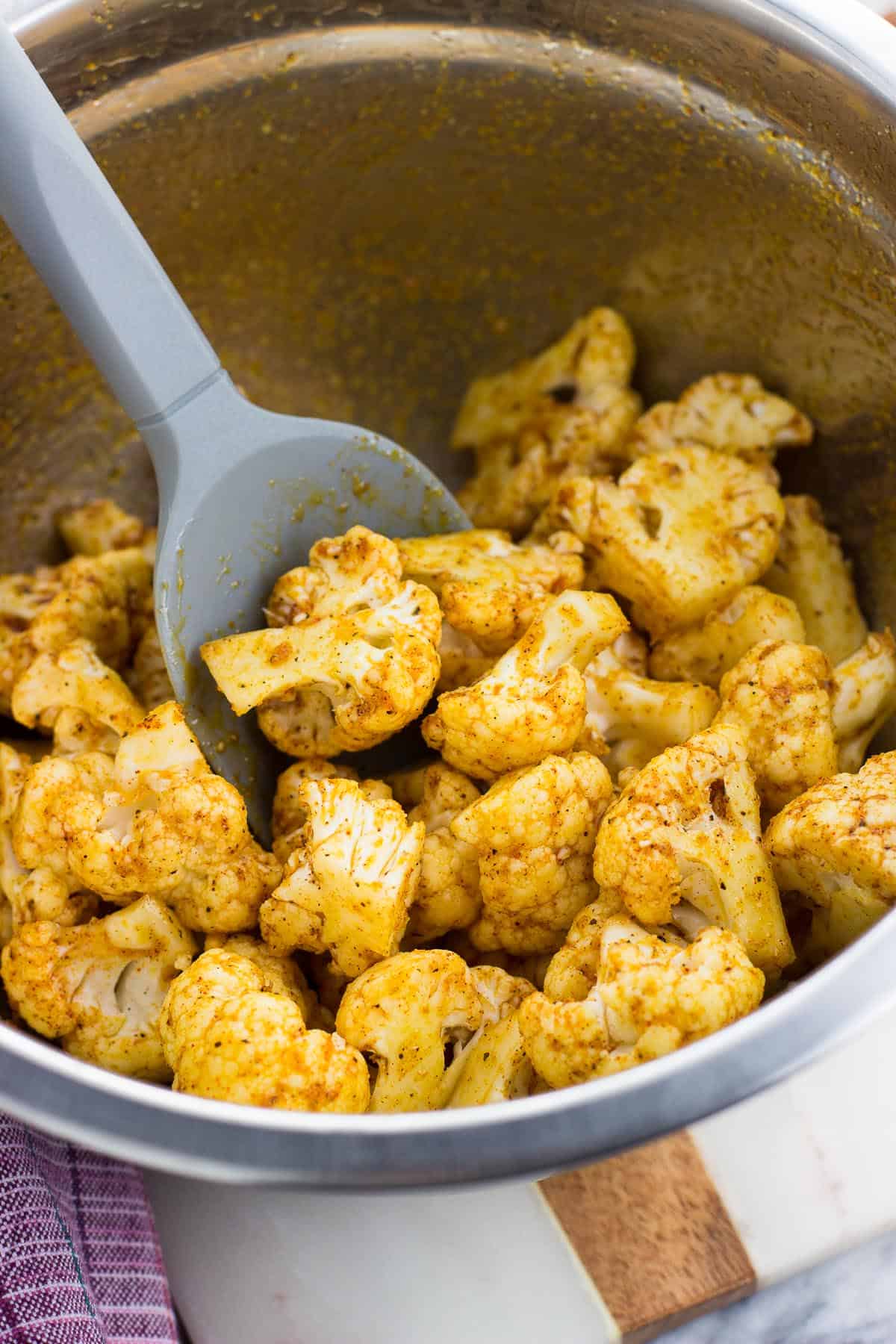 Cauliflower florets coated in oil and spices in a mixing bowl with a spatula.