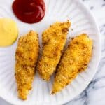 Three tenders on a plate with ketchup and mustard.