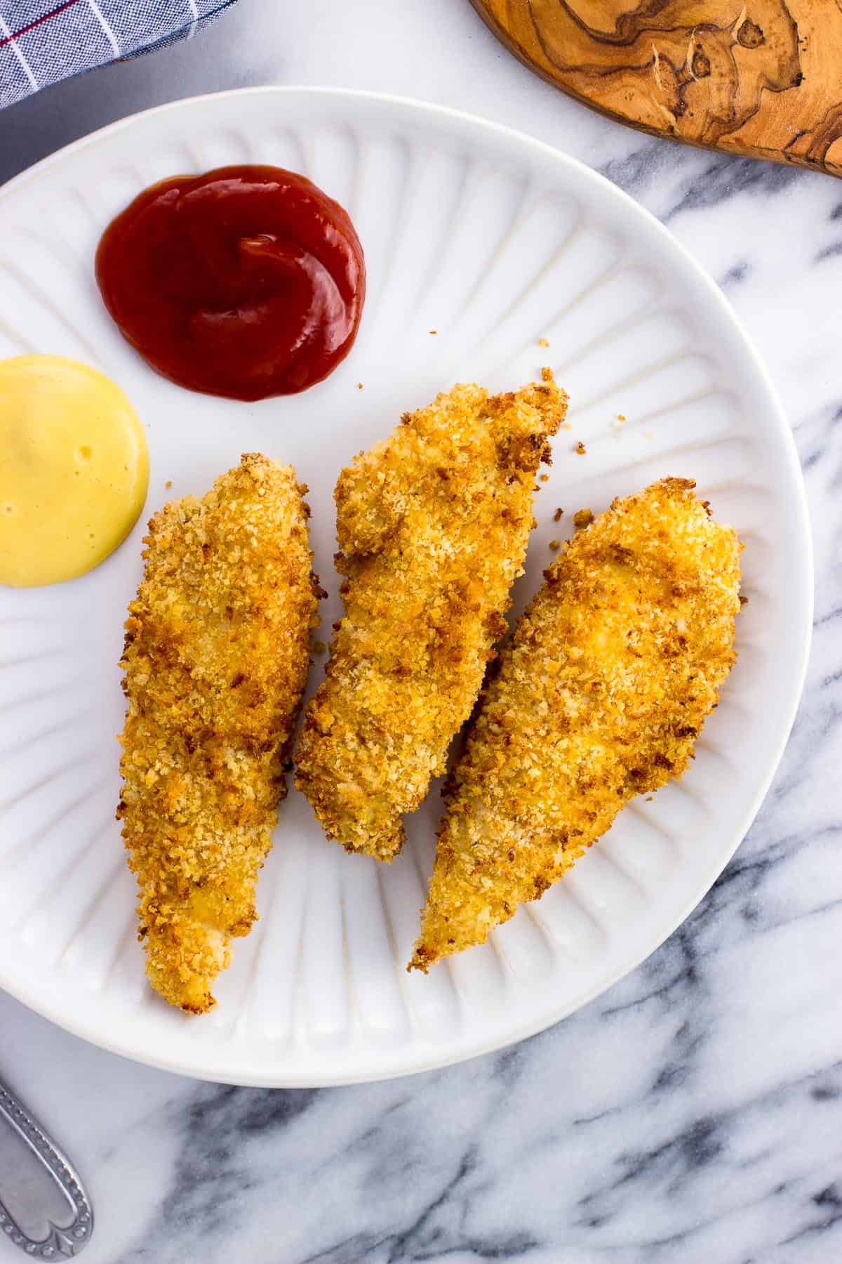 Three tenders on a plate with ketchup and mustard.