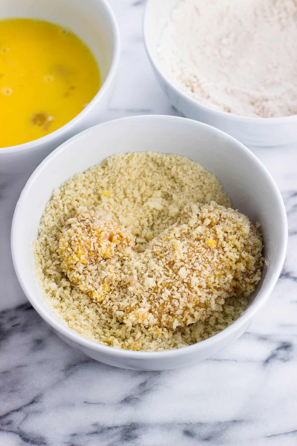 A chicken tender coated in panko in the bowl of panko.