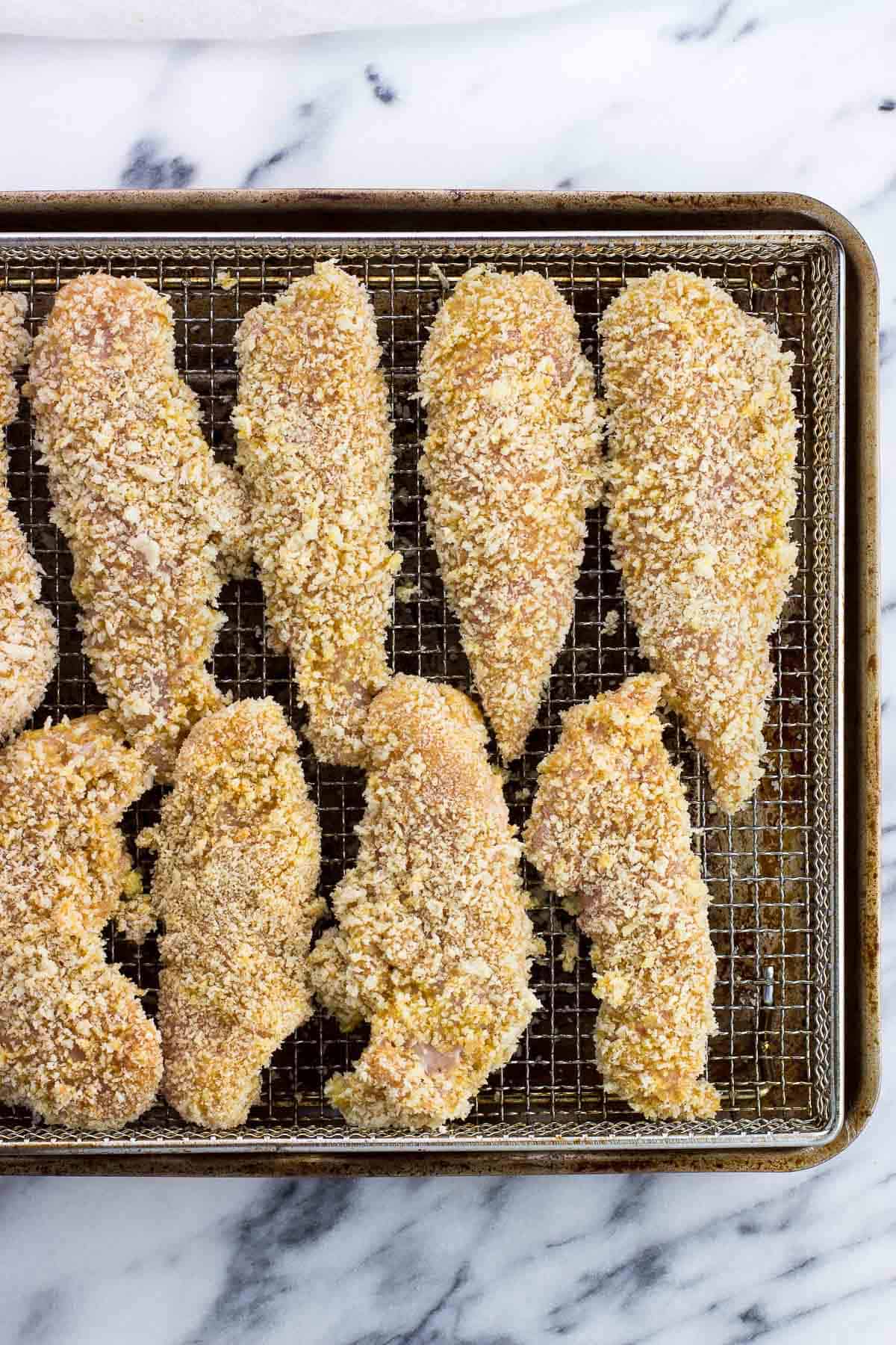 Raw breaded chicken tenders on an air fryer basket.