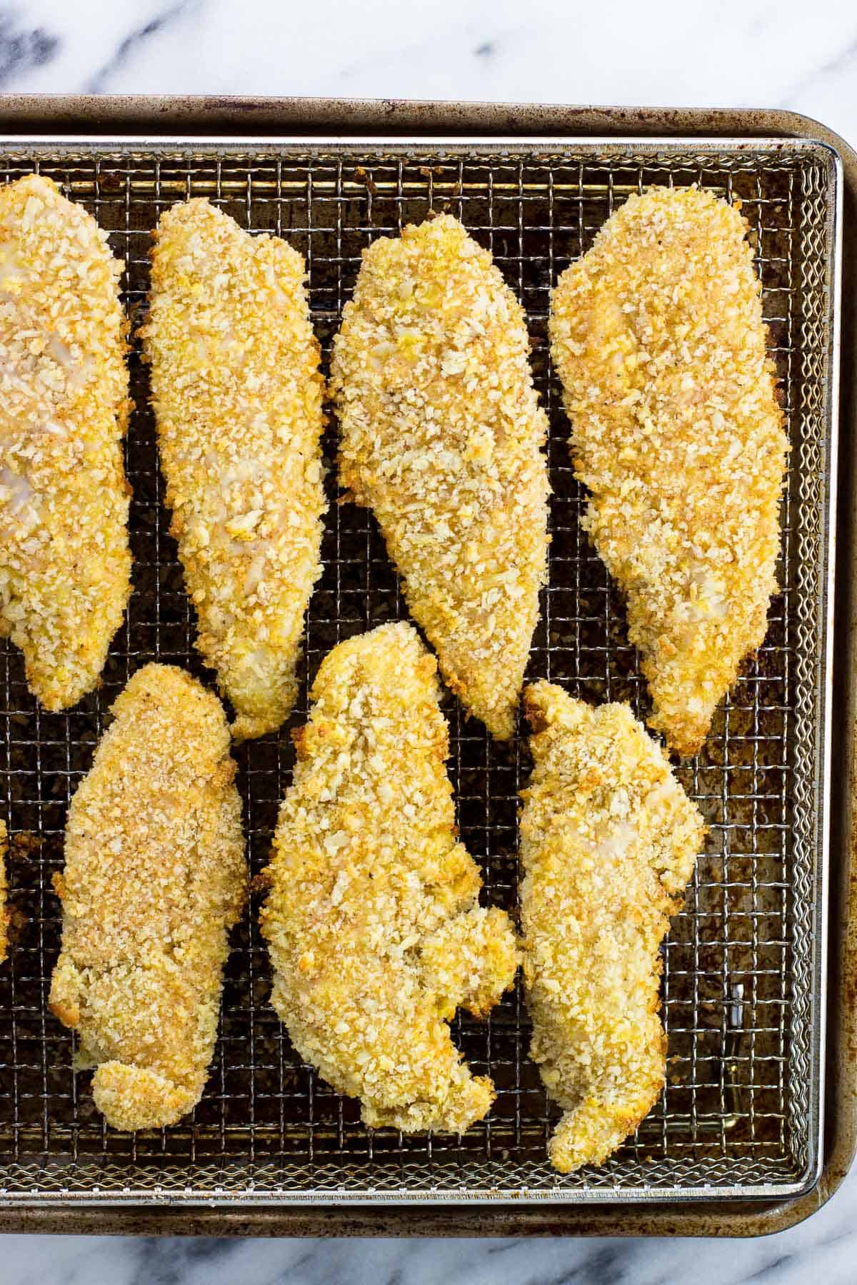 Coated chicken tenders on an air fryer basket halfway through cooking.