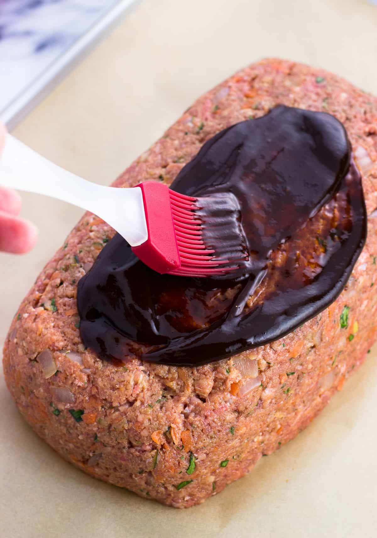 Balsamic ketchup being brushed onto a shaped meatloaf.