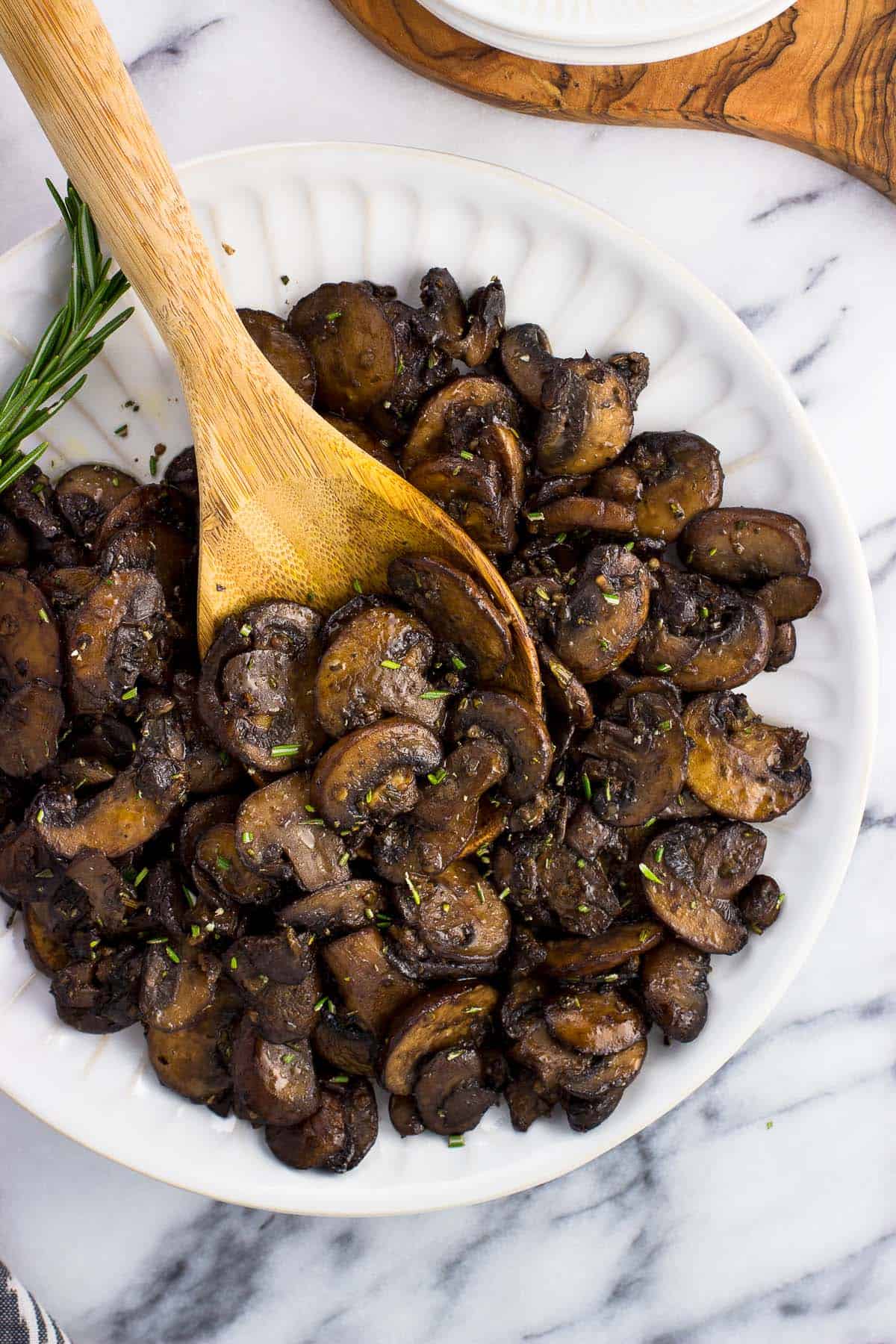 A wooden serving spoon in a pile of mushrooms on a plate.