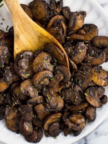 A wooden serving spoon in a pile of mushrooms on a plate.