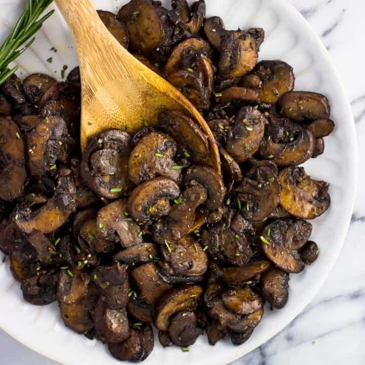 A wooden serving spoon in a pile of mushrooms on a plate.
