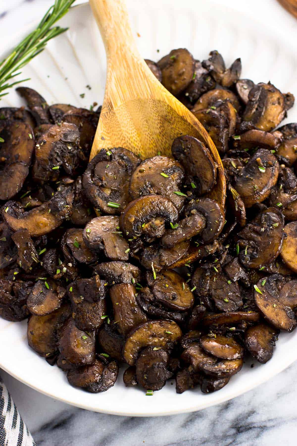 A wooden serving spoon in a pile of mushrooms on a plate.