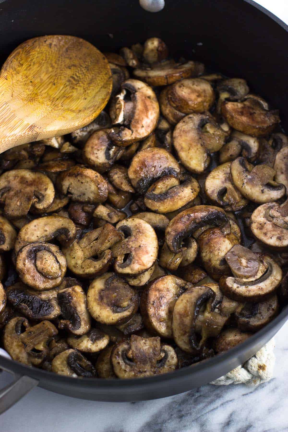 Mushrooms beginning the saute process in a pan with a wooden spoon.