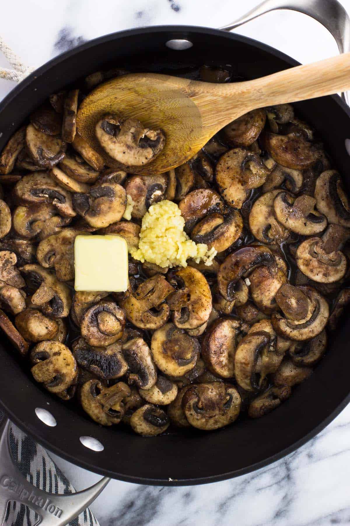 Butter and garlic added to the mushrooms in a pan.