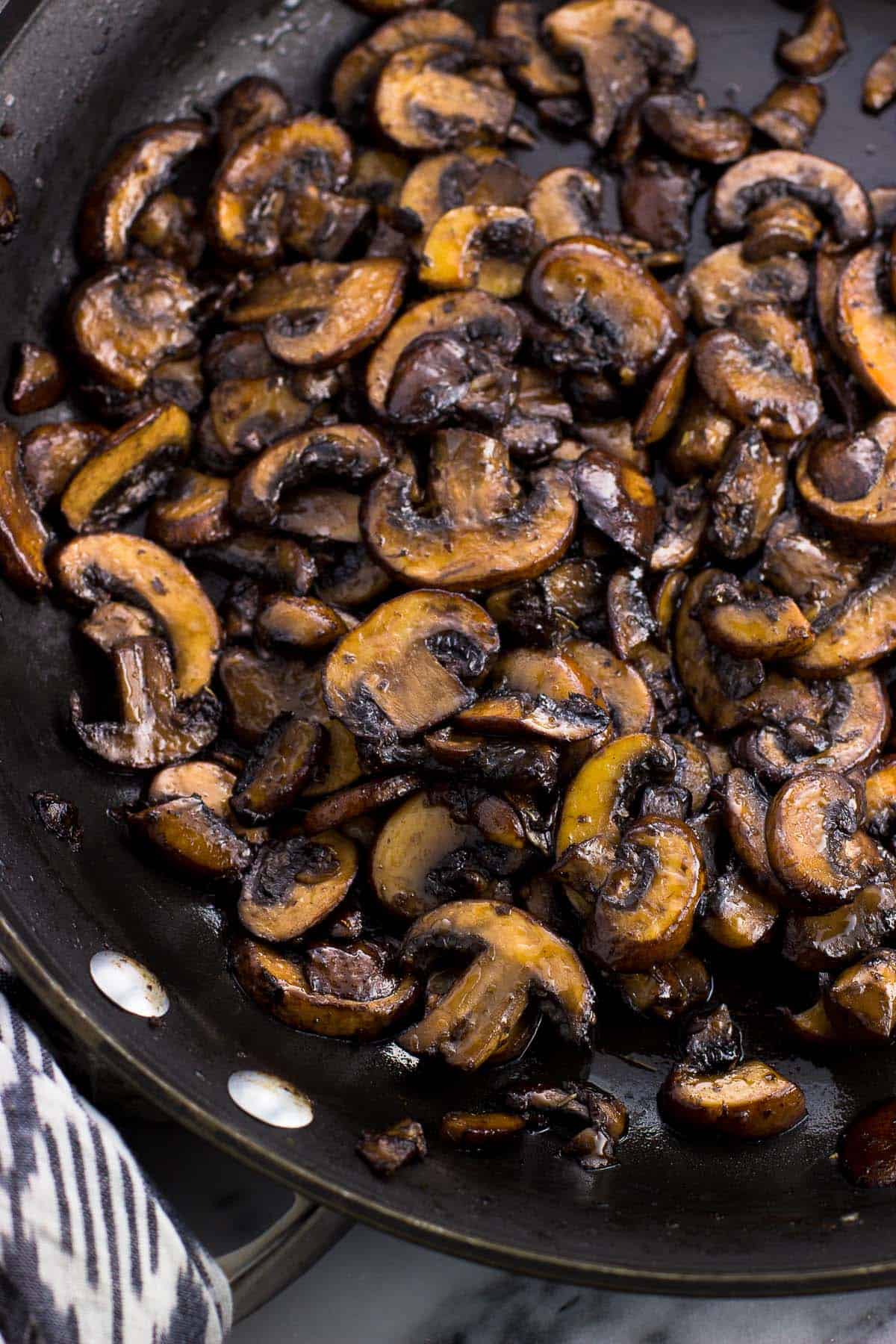 Sliced mushrooms near the end of the saute process in a large pan.