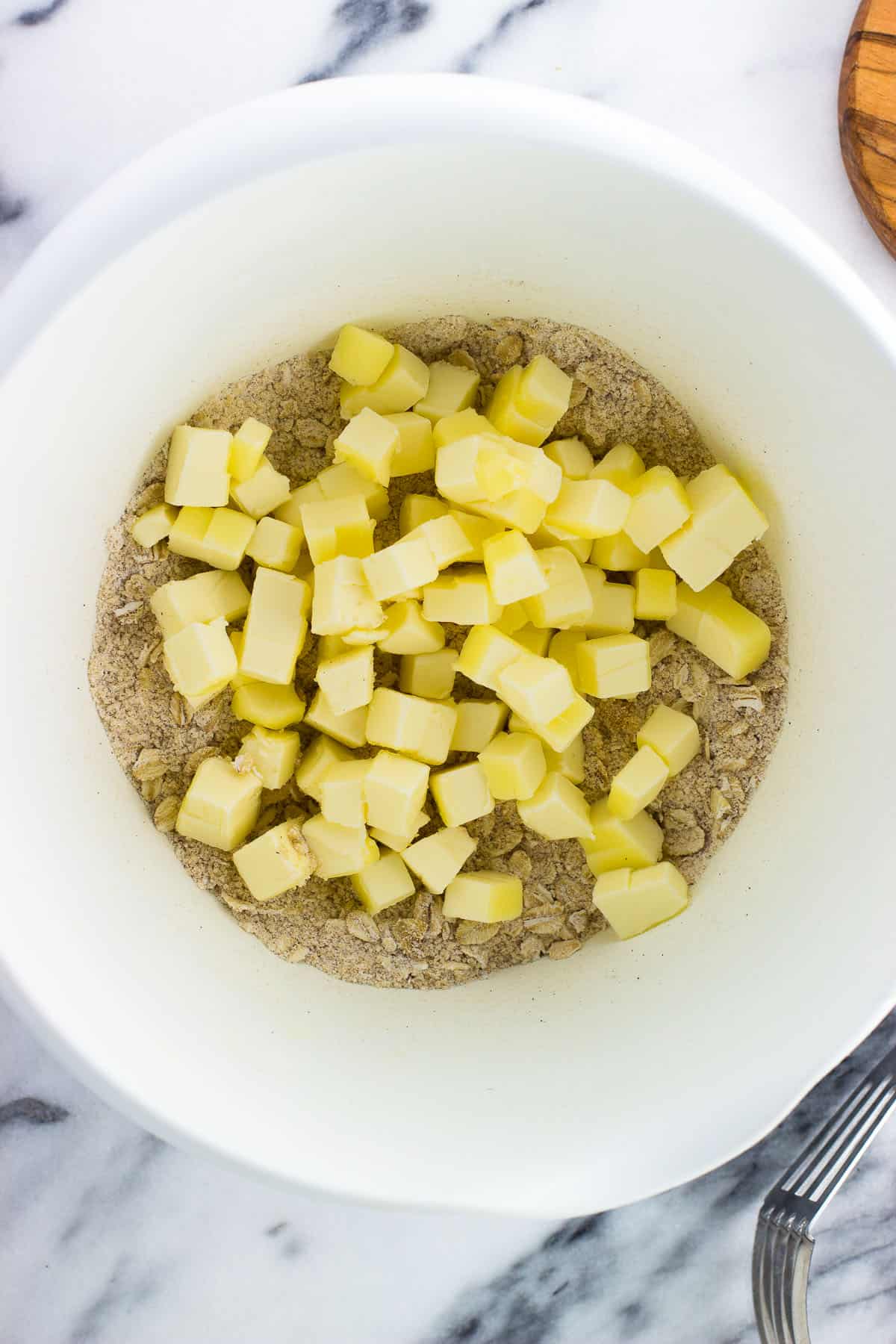 Cubed butter on top of the oat topping mixture in a bowl.