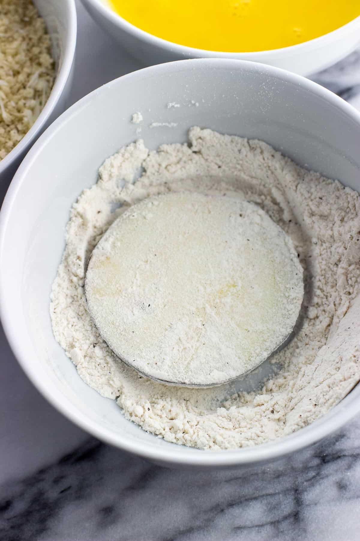 An eggplant round dredged in flour in the flour bowl.