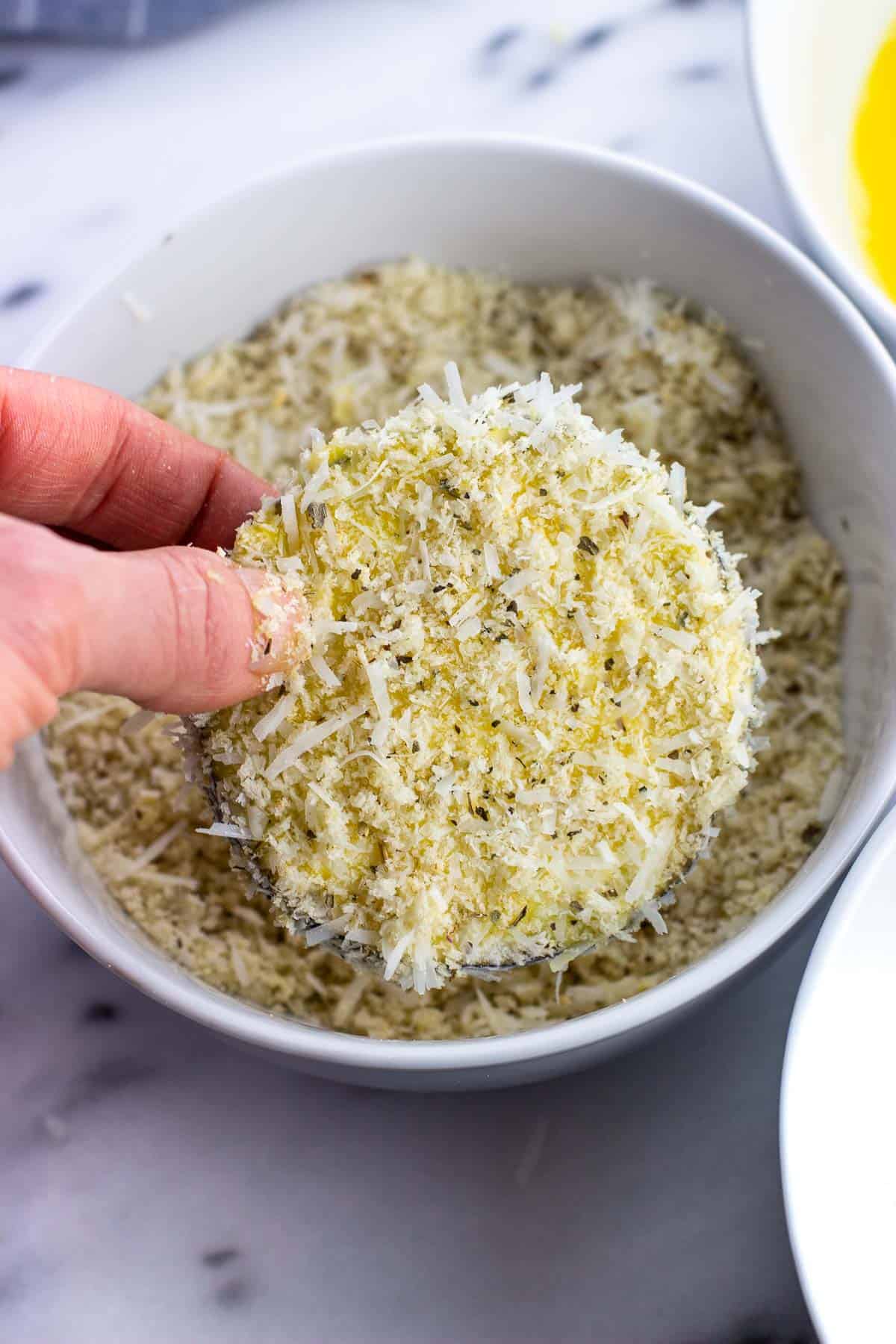 A hand holding an eggplant round covered in Parmesan and panko.