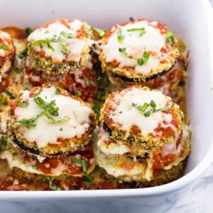 Cooked eggplant stacks in a baking dish topped with fresh basil.