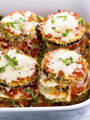 Cooked eggplant stacks in a baking dish topped with fresh basil.