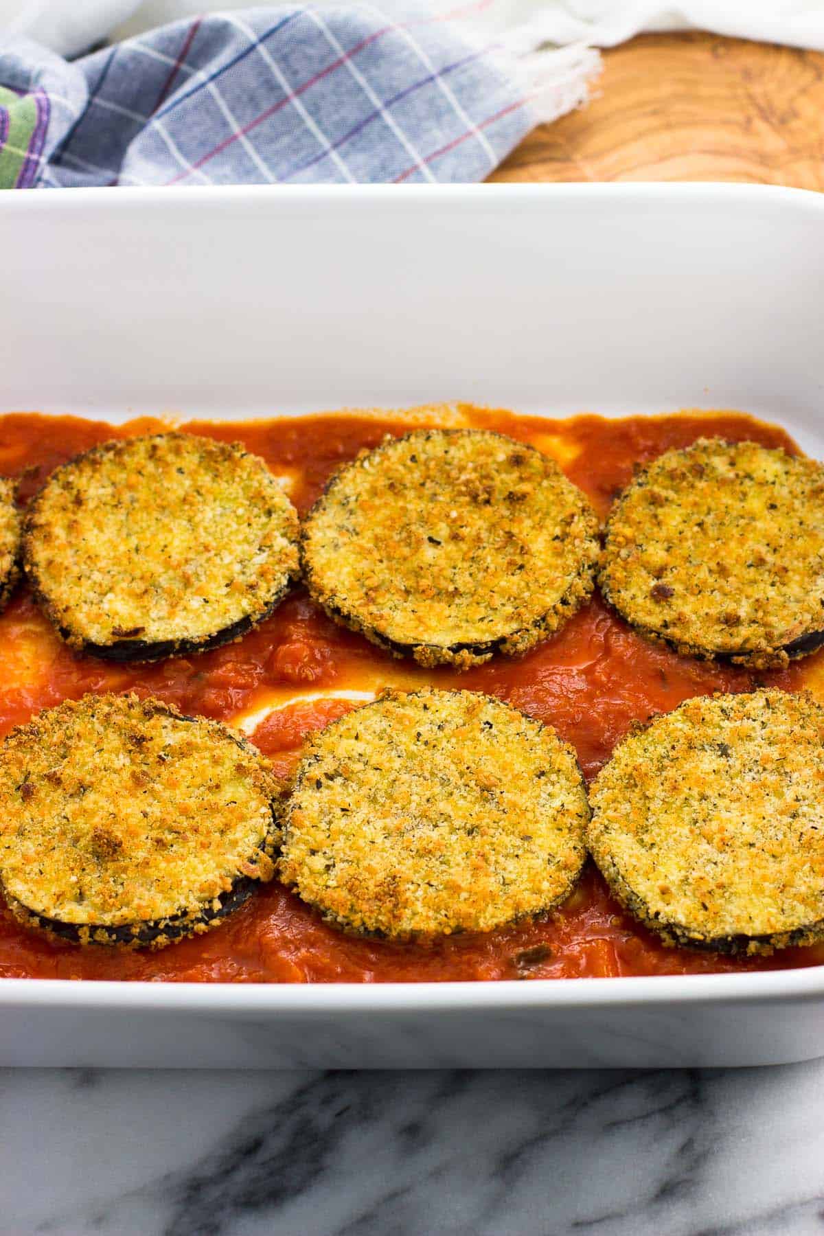 Eggplant rounds on a marinara sauce base in a large baking dish.