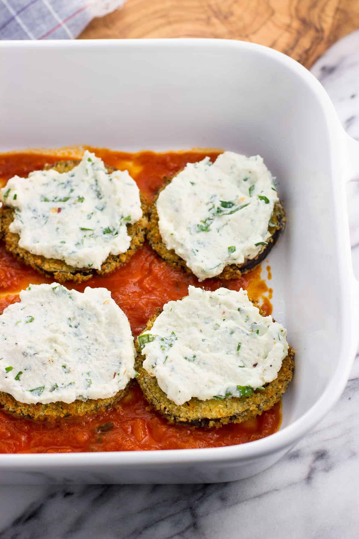 Ricotta spread on top of eggplant rounds in the assembly process.